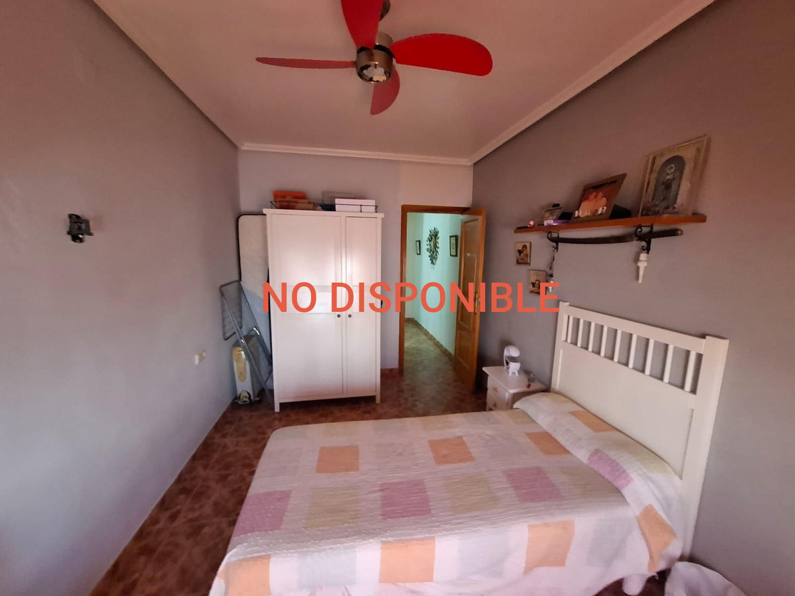Dormitorio con cama, armario blanco y puerta abierta a un pasillo. Ventilador de techo rojo.