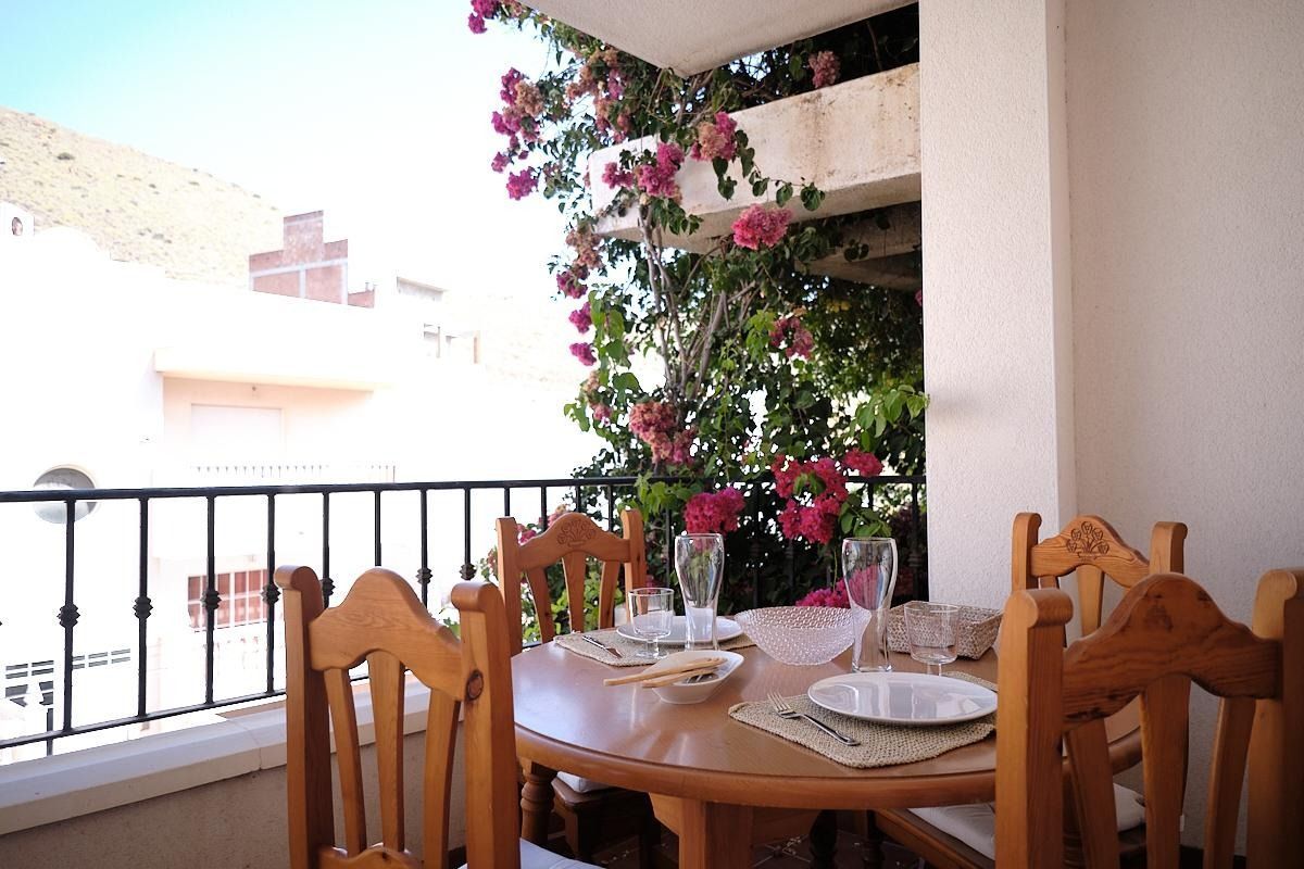 Una mesa y sillas en un balcón con flores al fondo.