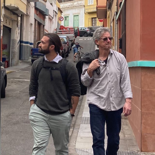 Dos hombres caminan por una calle estrecha y uno lleva una mochila en la espalda.