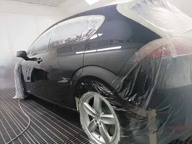 Un coche negro se encuentra en una cabina de pintura con las ventanas 