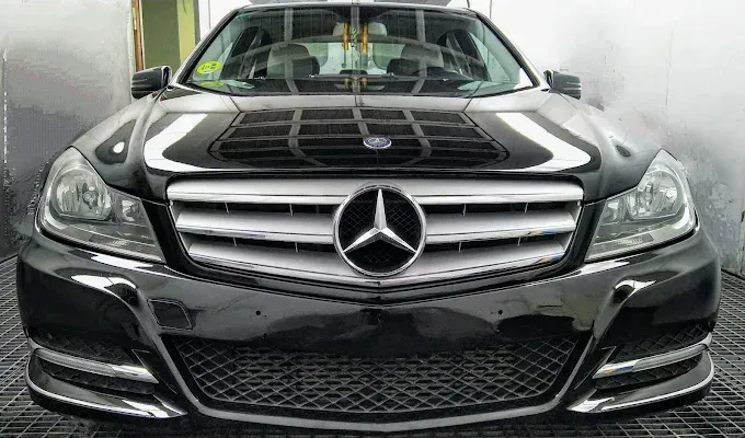 Vista frontal de un sedán Mercedes-Benz negro con un prominente logotipo de estrella de tres puntas en la parrilla.