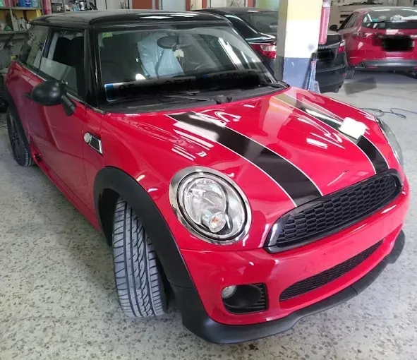Un MINI Cooper rojo con franjas de carreras negras y techo negro, estacionado en un garaje cubierto.