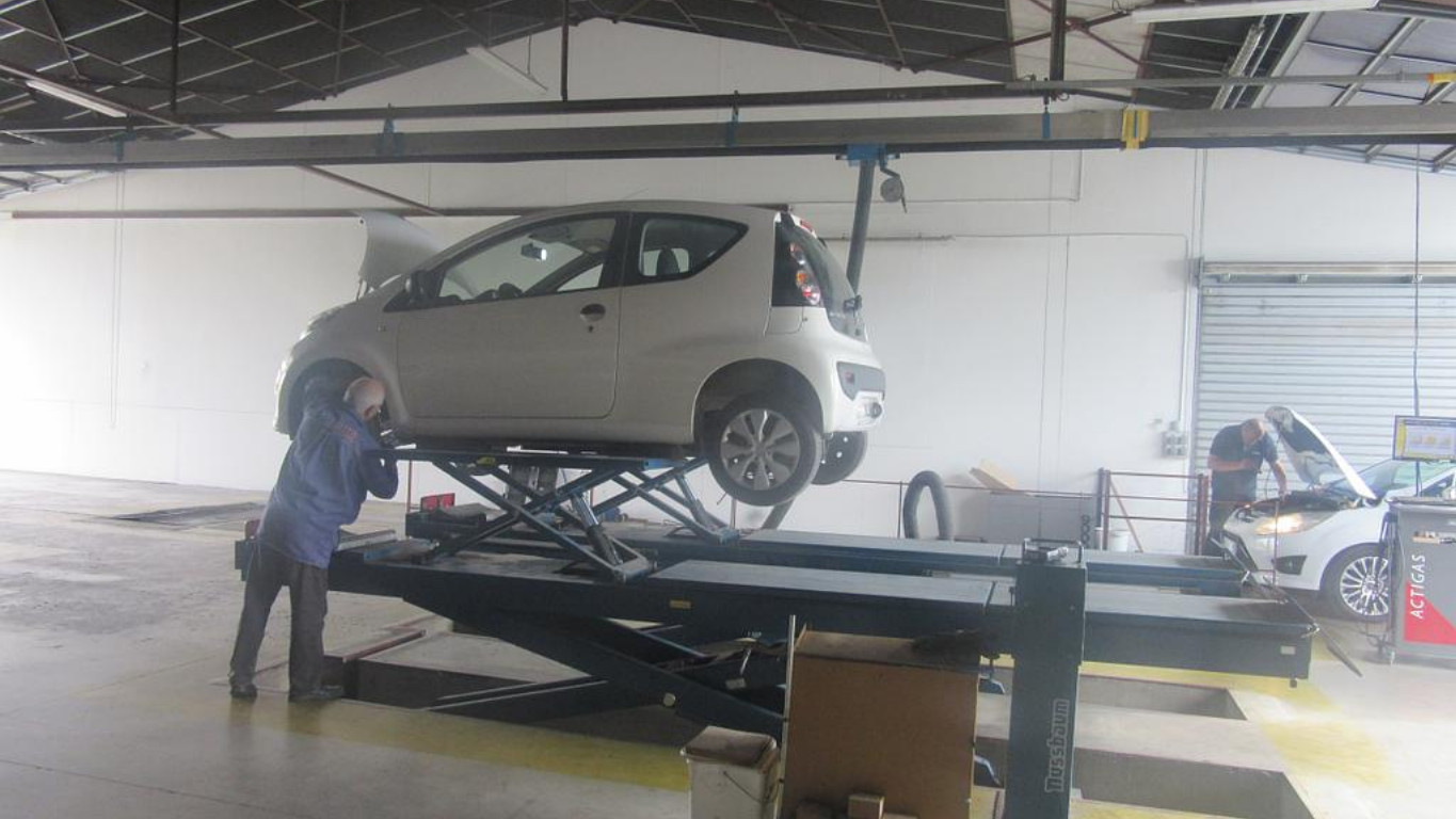 Voiture sur un pont élévateur avec un technicien réalisant un contrôle.