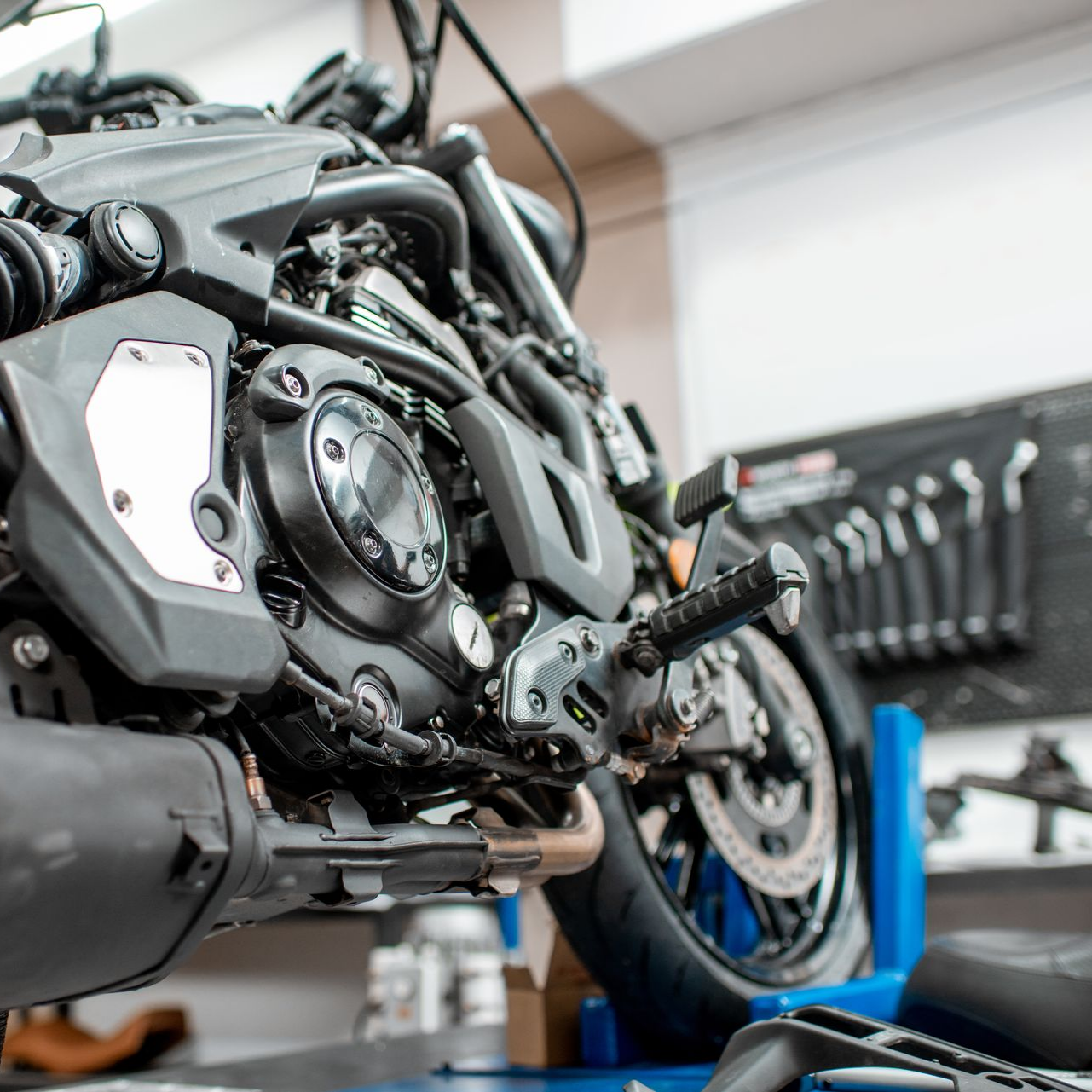 Gros plan sur le moteur et la roue d'une moto dans un atelier de réparation, sur un support bleu, outils accrochés au mur.