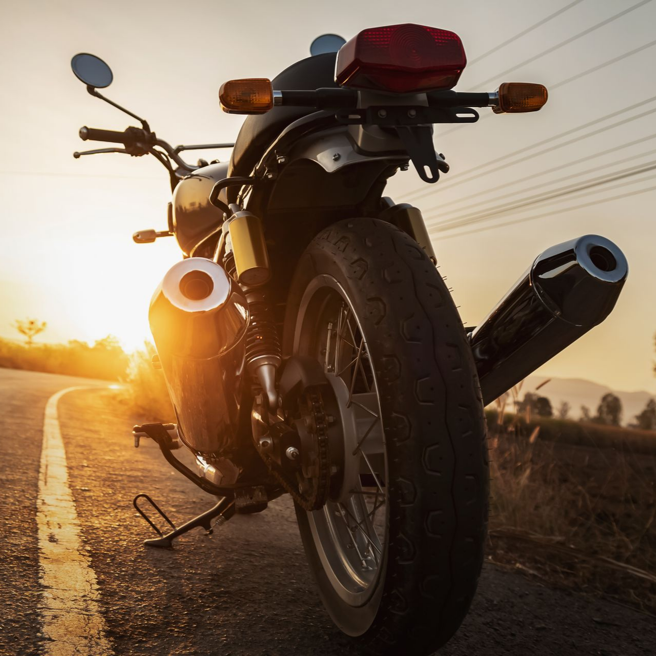 Vue arrière d’une moto arrêtée sur une route au soleil couchant.