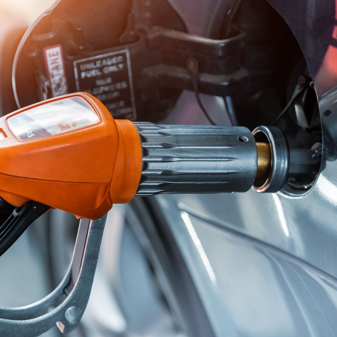 Pistolet de pompe à carburant dans le réservoir d'une voiture, poignée orange, embout gris.