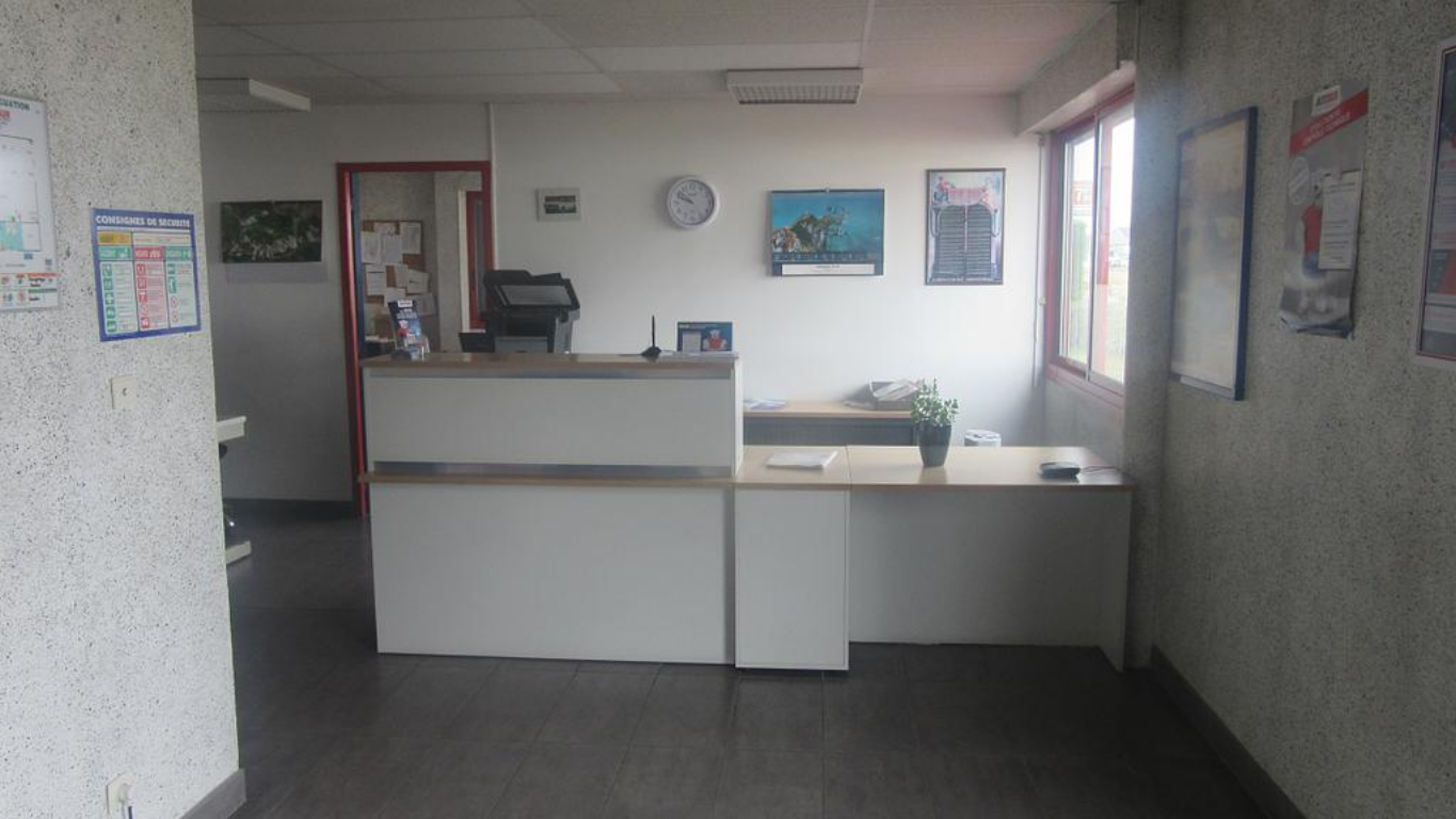 Comptoir d’accueil du centre avec documents, plante et affichages muraux.