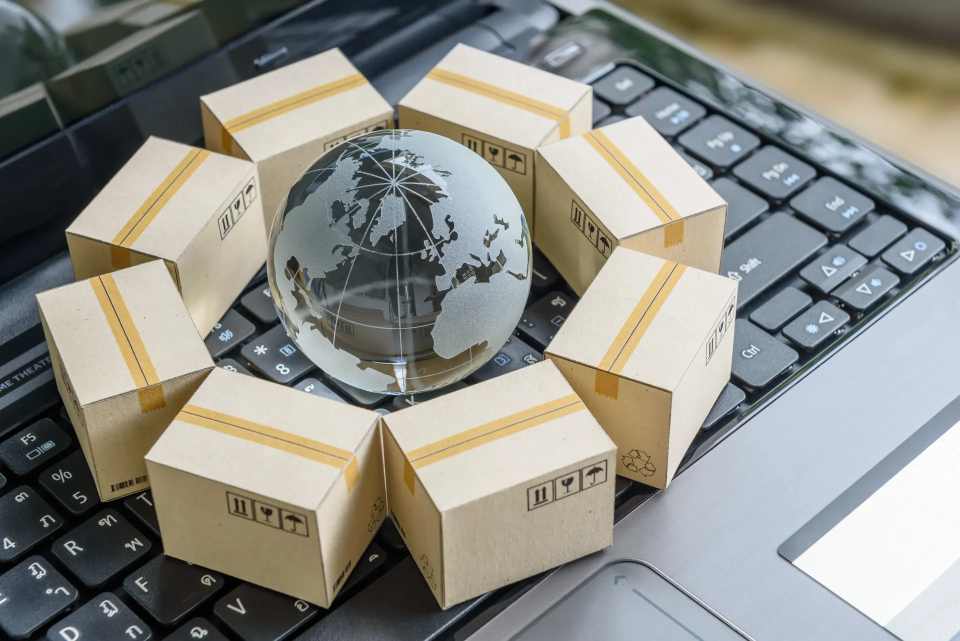 Un globo terráqueo está rodeado de cajas de cartón sobre un teclado de computadora portátil.