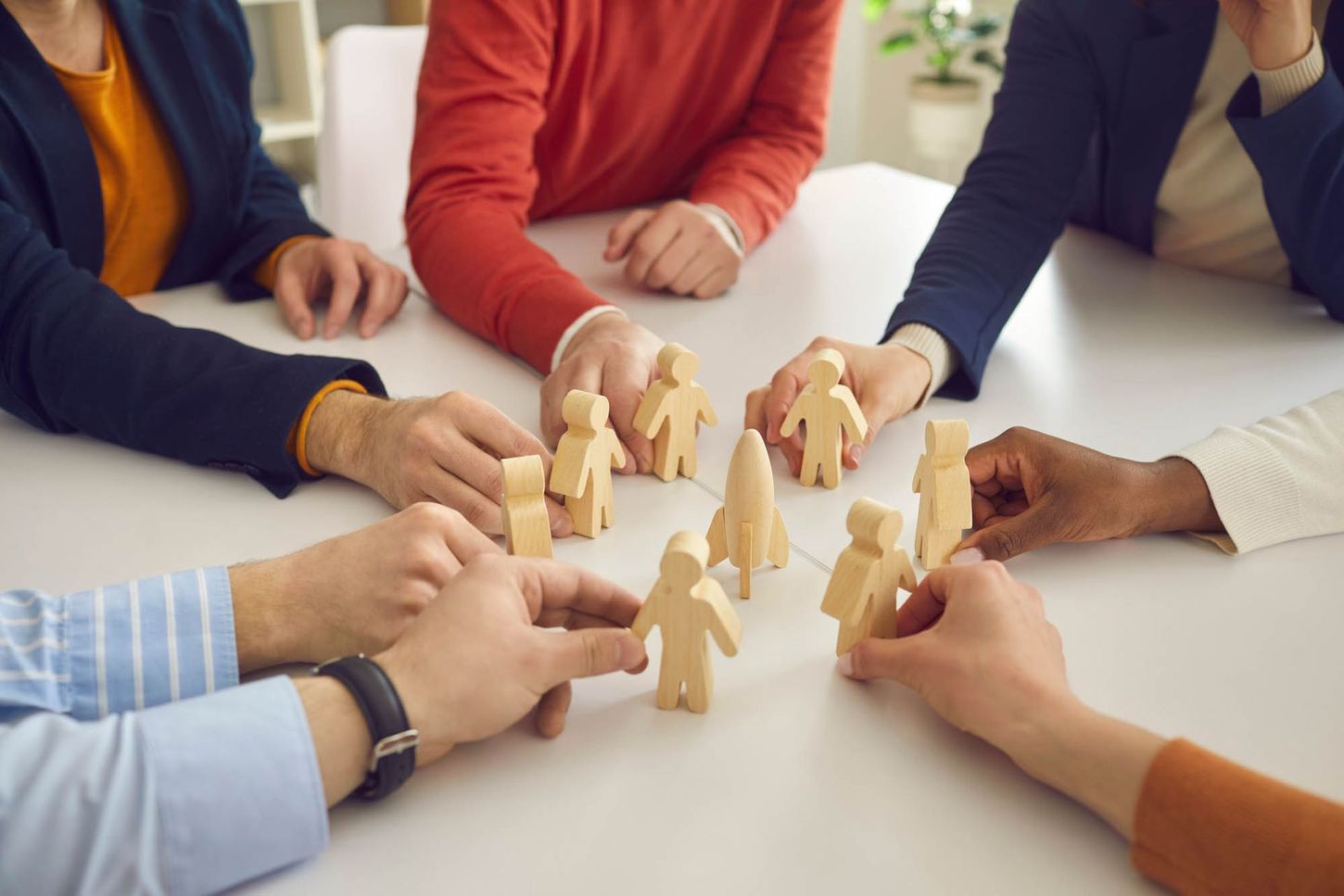 Eine Gruppe von Menschen sitzt um einen Tisch und hält Holzfiguren in den Händen.