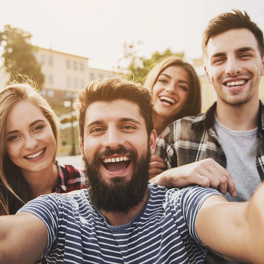 Cuatro amigos sonrientes tomándose un selfie al aire libre.