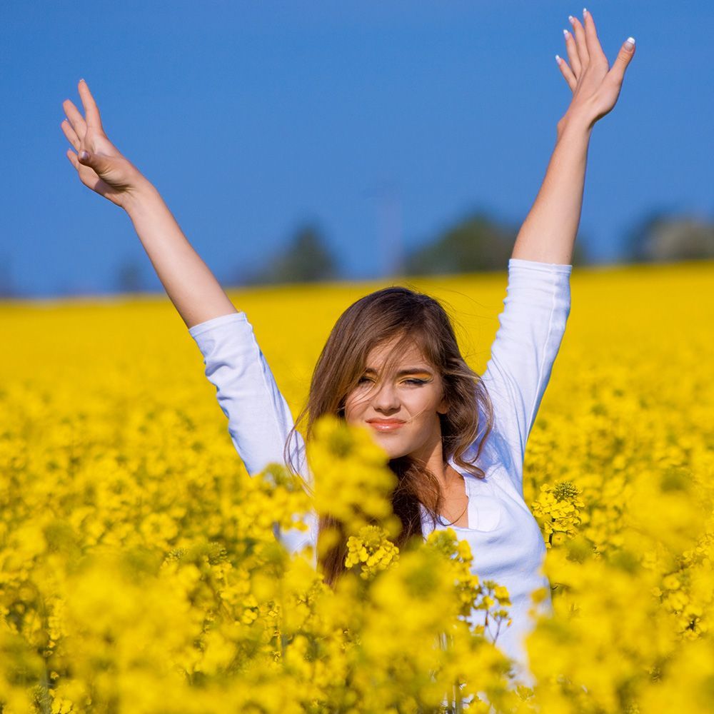 Mujer con los brazos levantados en un campo de flores amarillas, cielo azul de fondo.