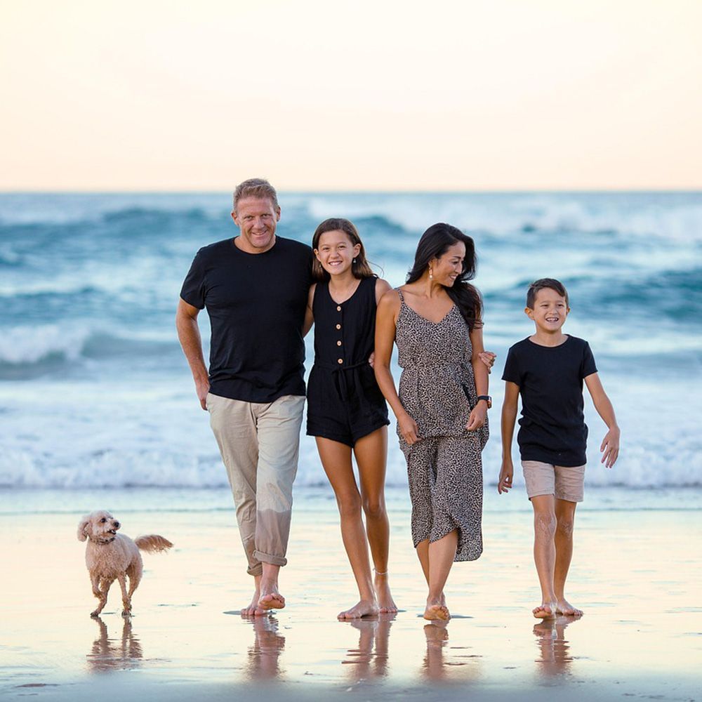 Familia de cuatro y un perro paseando por una playa al atardecer.
