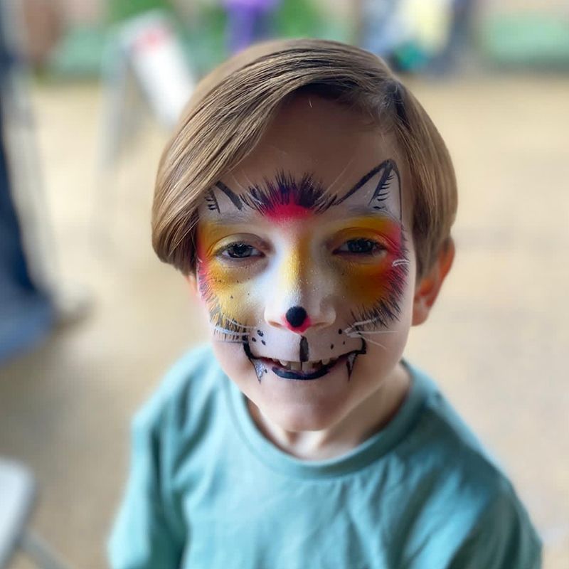 Niño con cara de lobo pintada de colores, sonriendo, afuera.