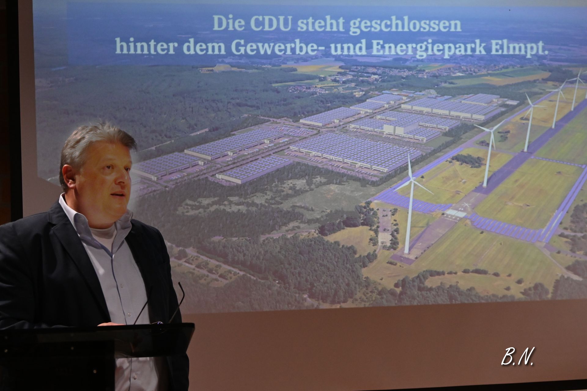 Ein Mann steht vor einer Projektionsleinwand, auf der ein Bild von Windmühlen zu sehen ist.
