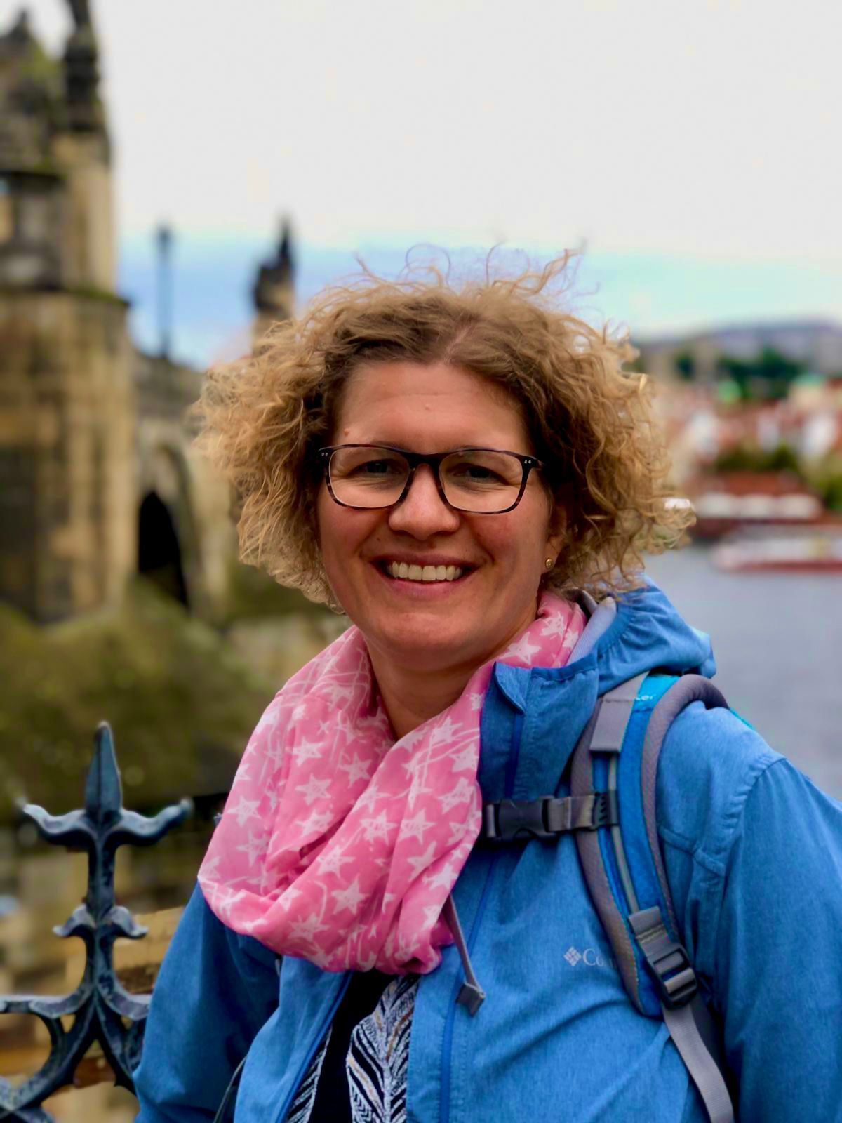 Eine Frau mit Brille und rosa Schal lächelt in die Kamera.