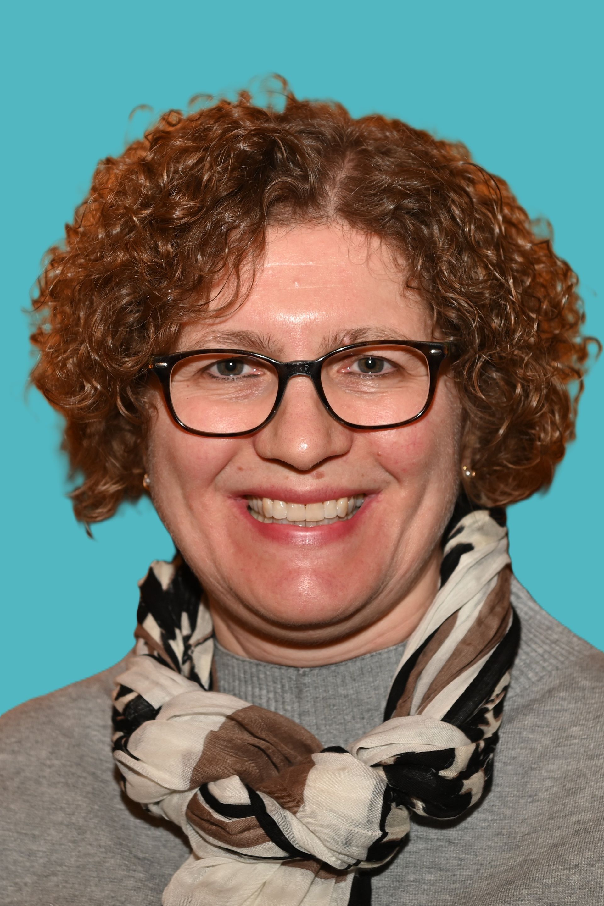 Eine Frau mit Brille und rosa Schal lächelt in die Kamera.