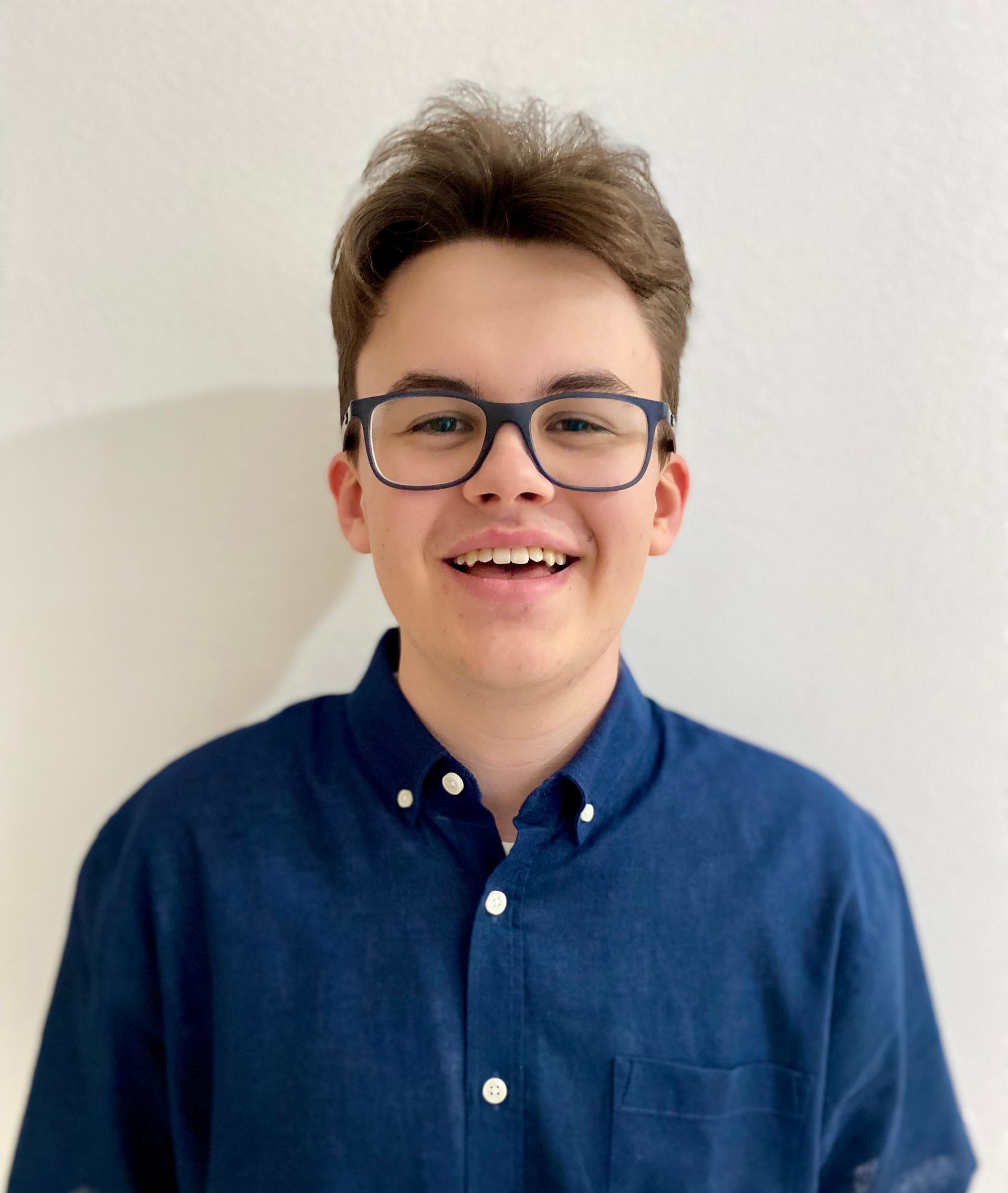 Ein junger Mann mit Brille und blauem Hemd lächelt in die Kamera.