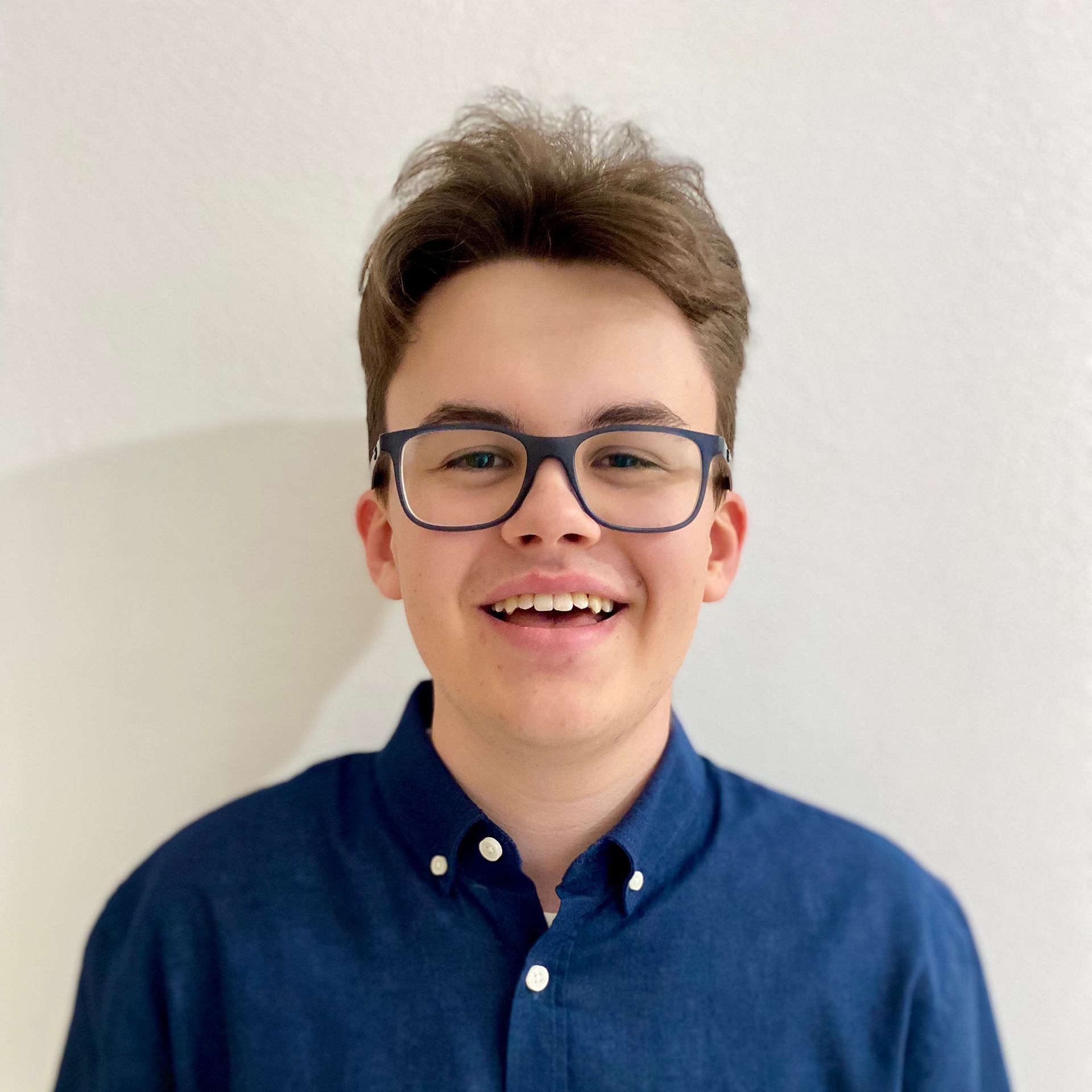Ein junger Mann mit Brille und blauem Hemd lächelt in die Kamera.