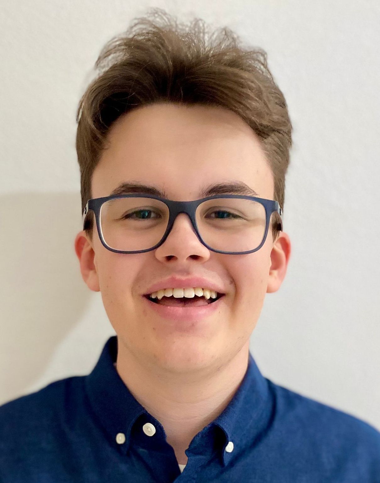 Ein junger Mann mit Brille und blauem Hemd lächelt in die Kamera.