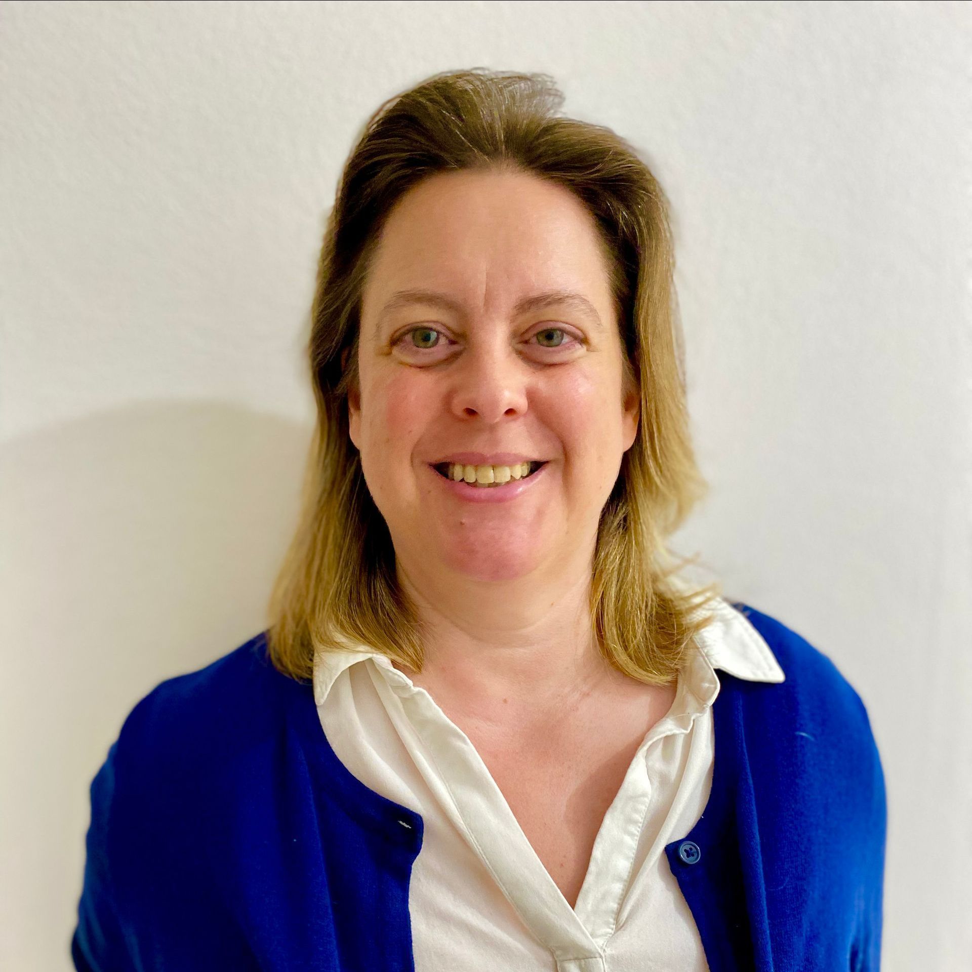 Eine Frau in einer blauen Strickjacke und einem weißen Hemd lächelt in die Kamera