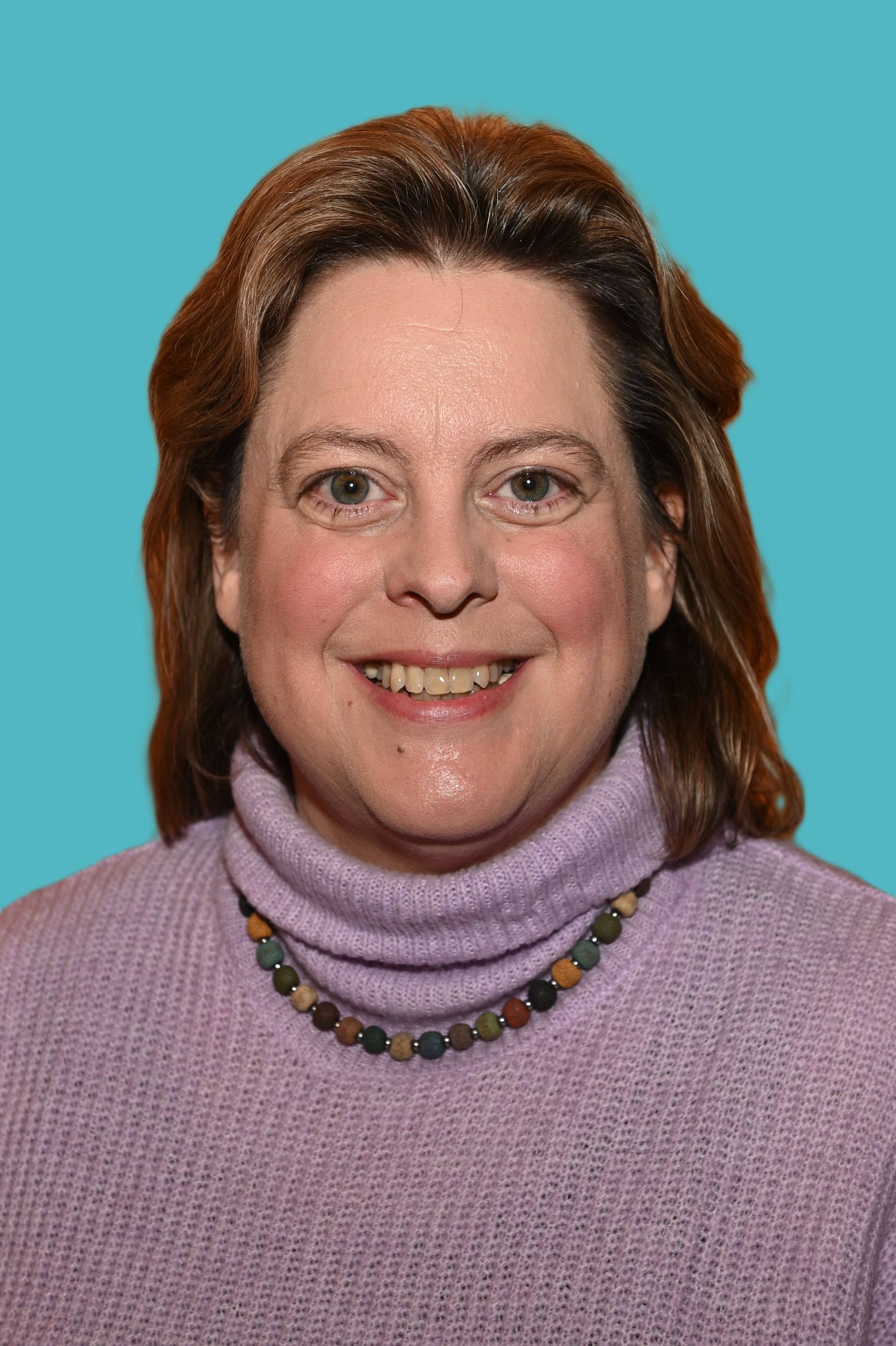 Eine Frau in einer blauen Strickjacke und einem weißen Hemd lächelt in die Kamera