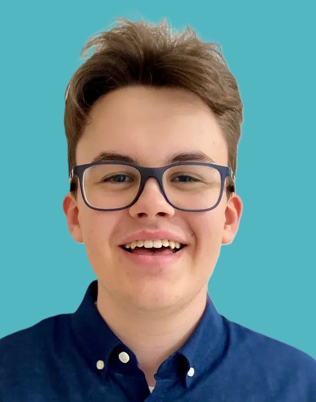 Ein junger Mann mit Brille und blauem Hemd lächelt in die Kamera.