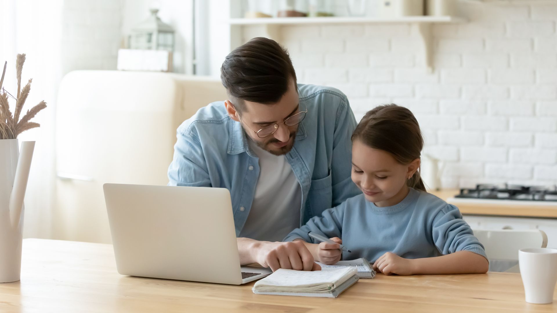 Un hombre y una niña están sentados en una mesa con una computadora portátil.
