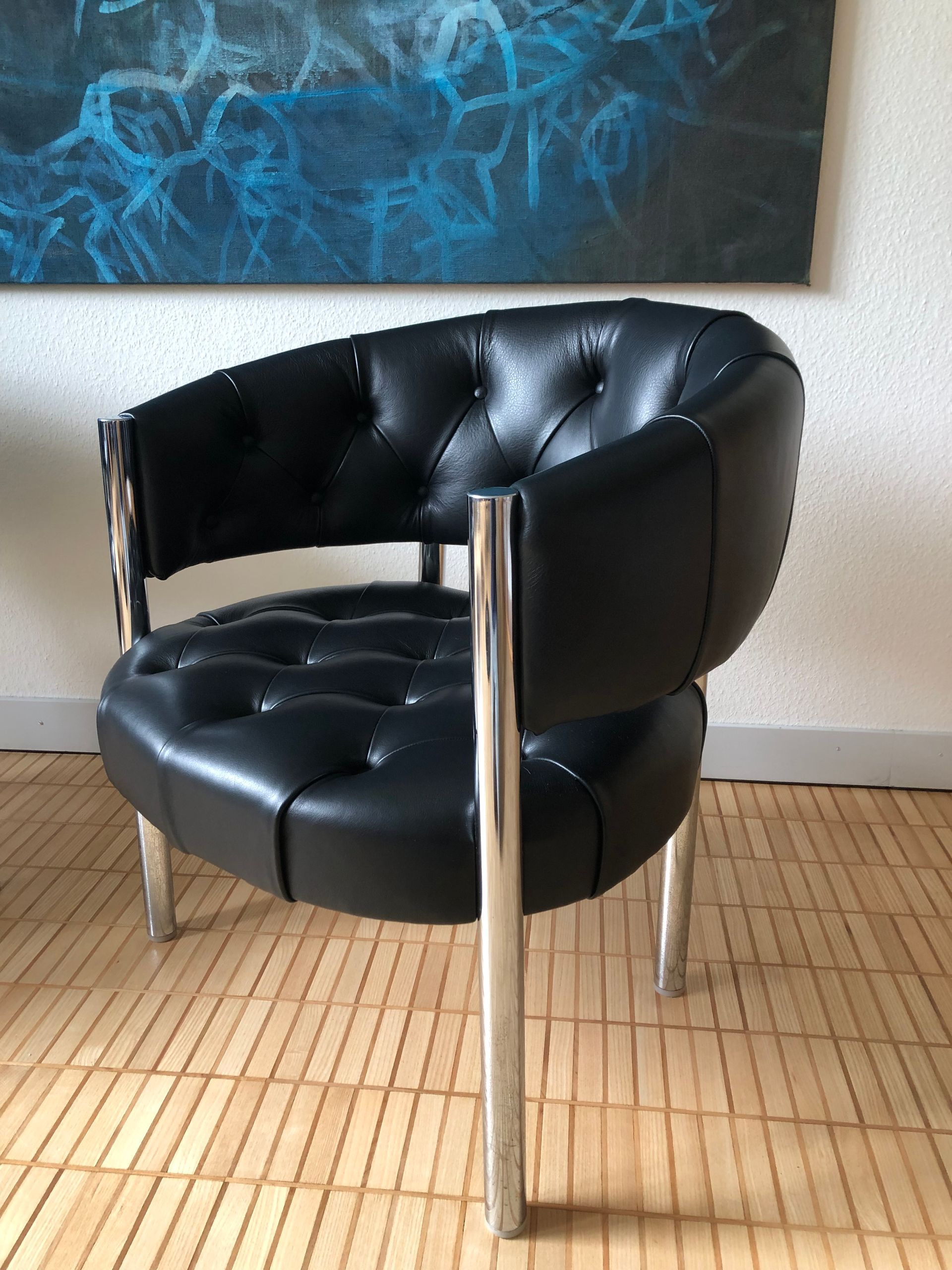 Ein schwarzer Ledersessel steht vor einem Gemälde an der Wand.