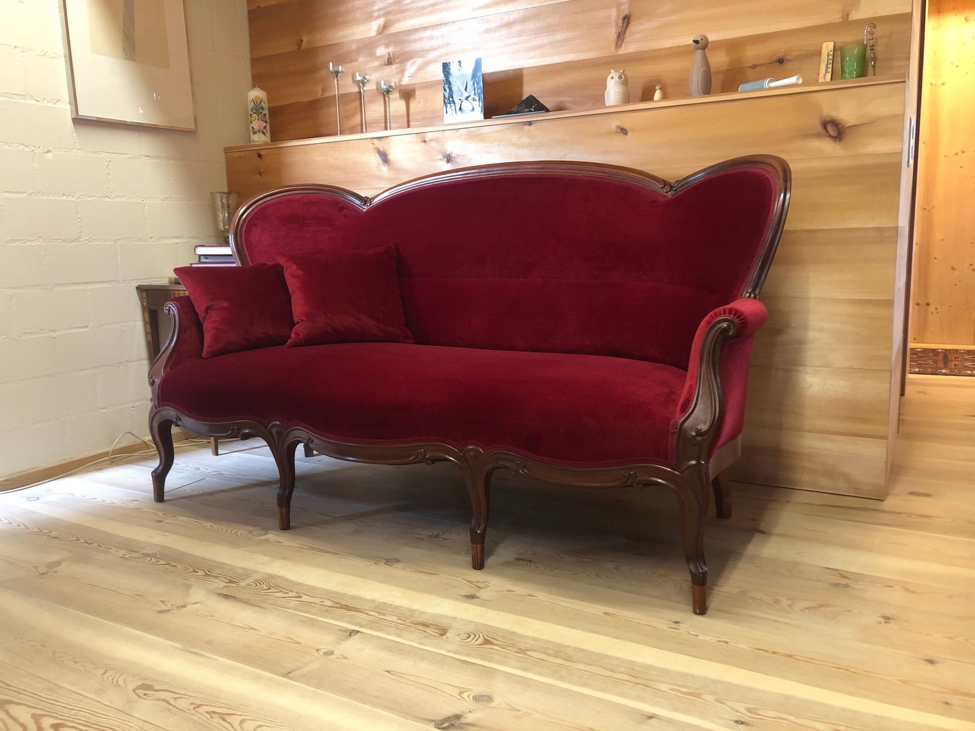 In einem Zimmer steht ein rotes Sofa auf einem Holzboden.