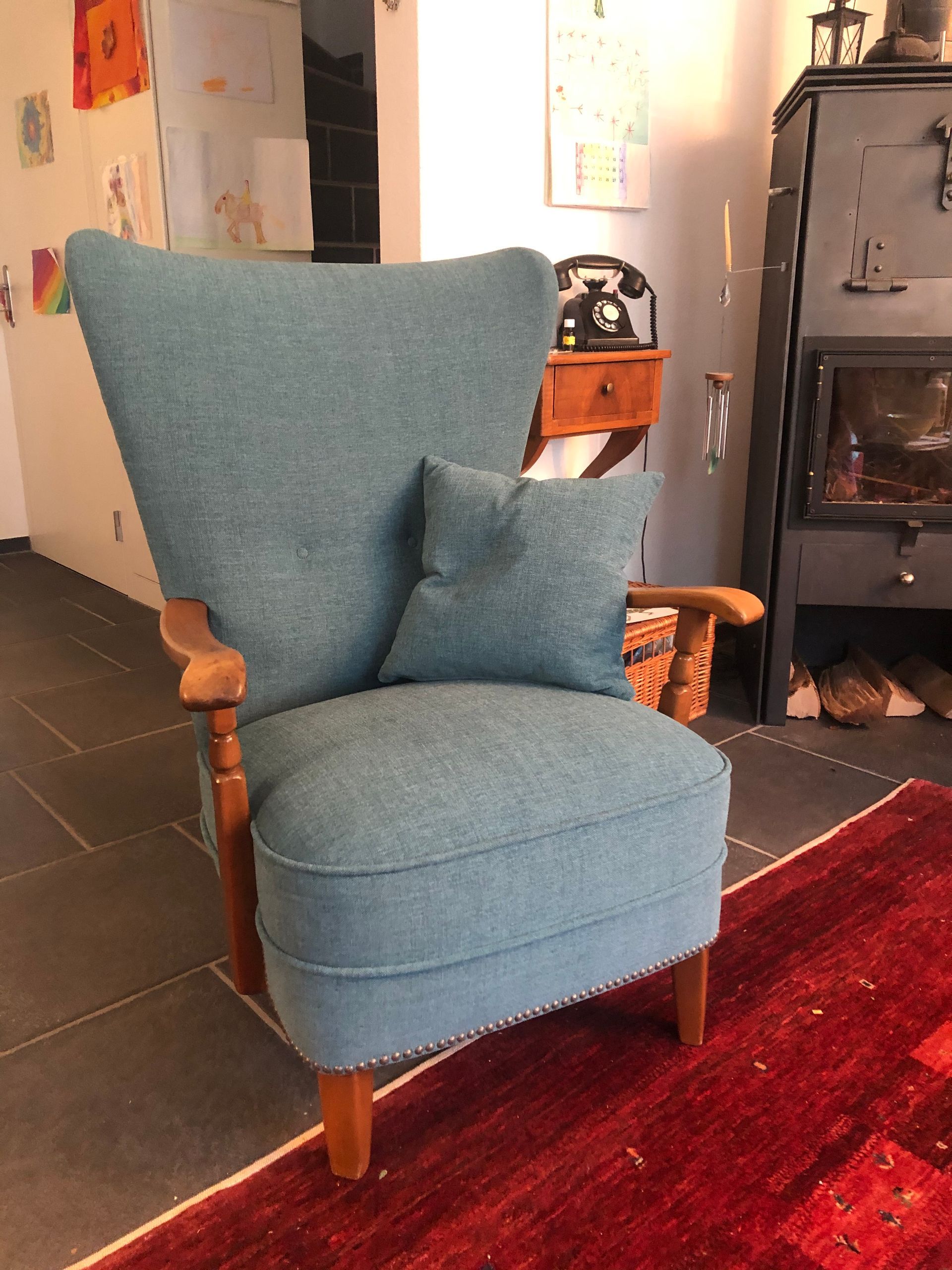 Ein blauer Stuhl mit einem Kissen darauf steht auf einem roten Teppich in einem Wohnzimmer.