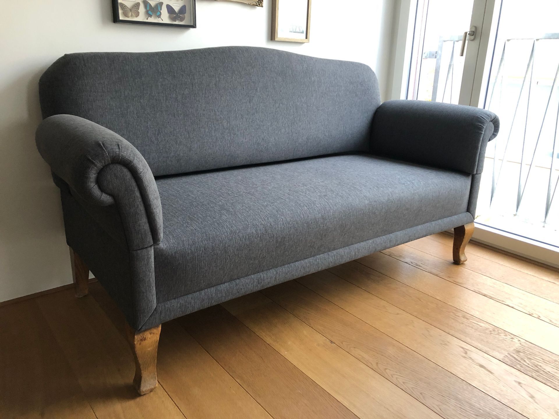 Ein graues Sofa steht auf einem Holzboden vor einem Fenster.