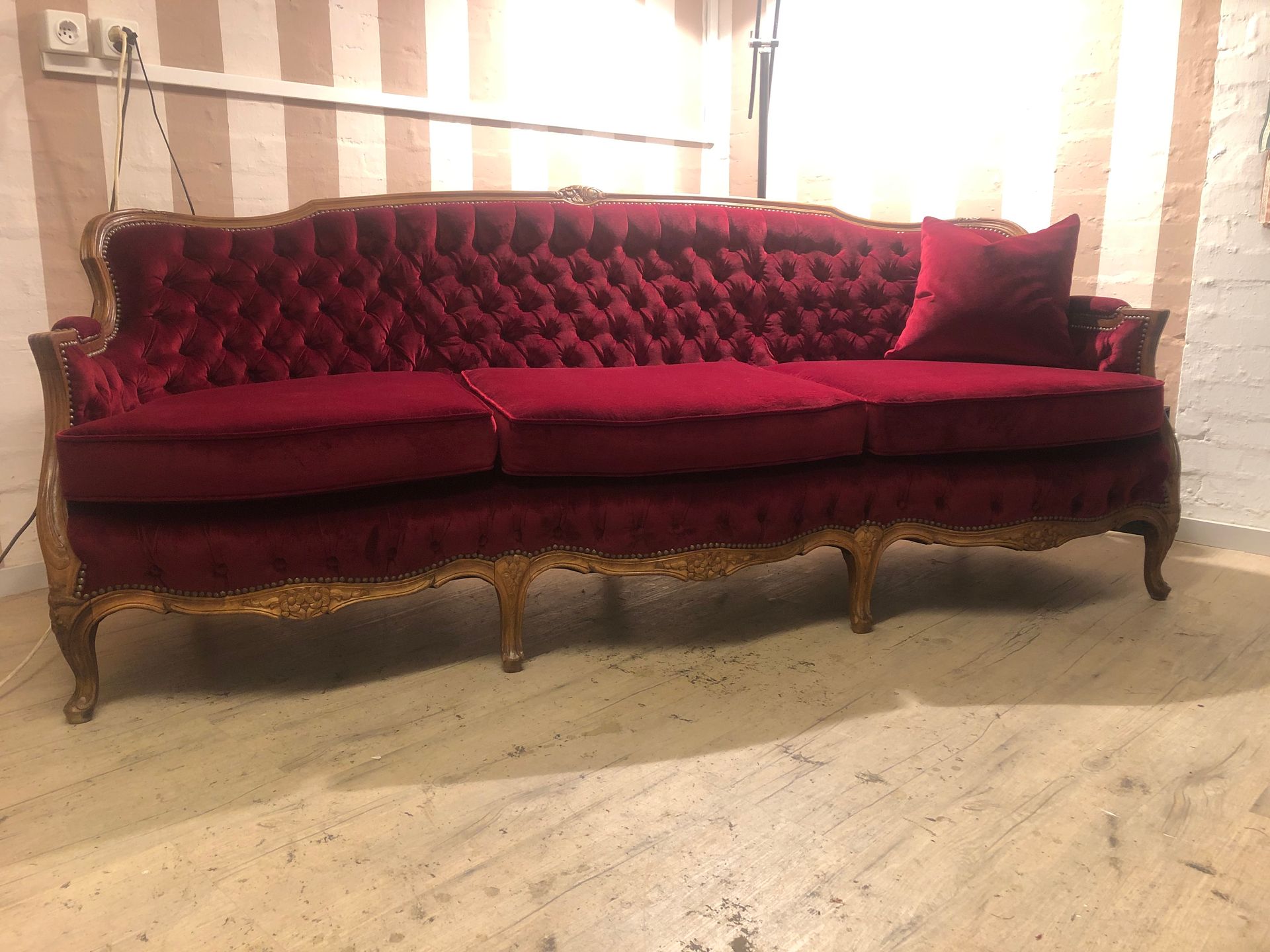 In einem Raum mit gestreifter Wand steht ein langes rotes Sofa.