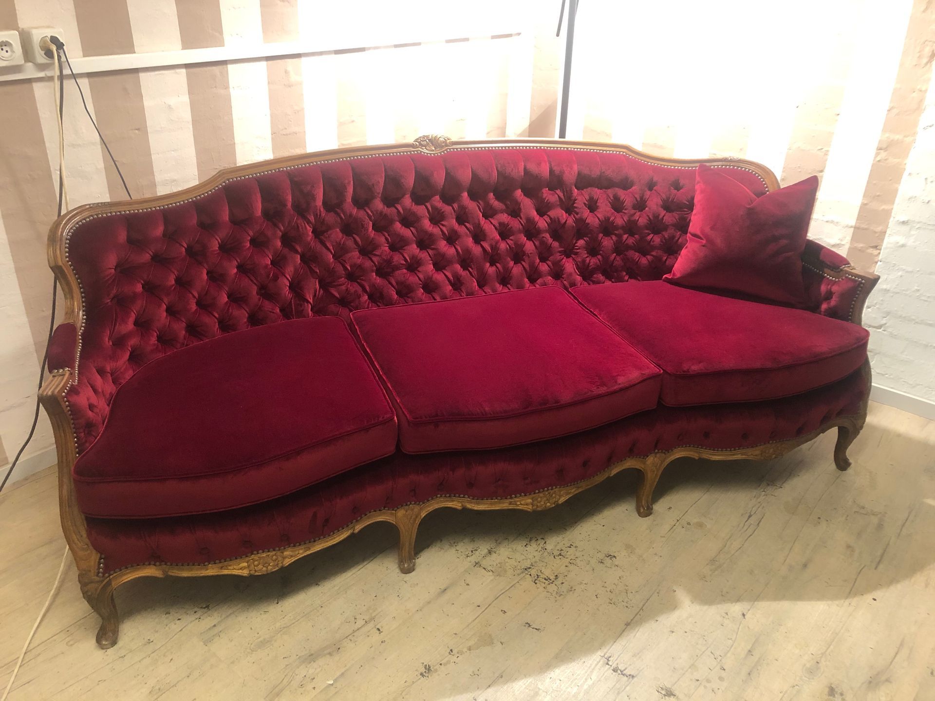 In einem Zimmer steht ein rotes Sofa auf einem Holzboden.
