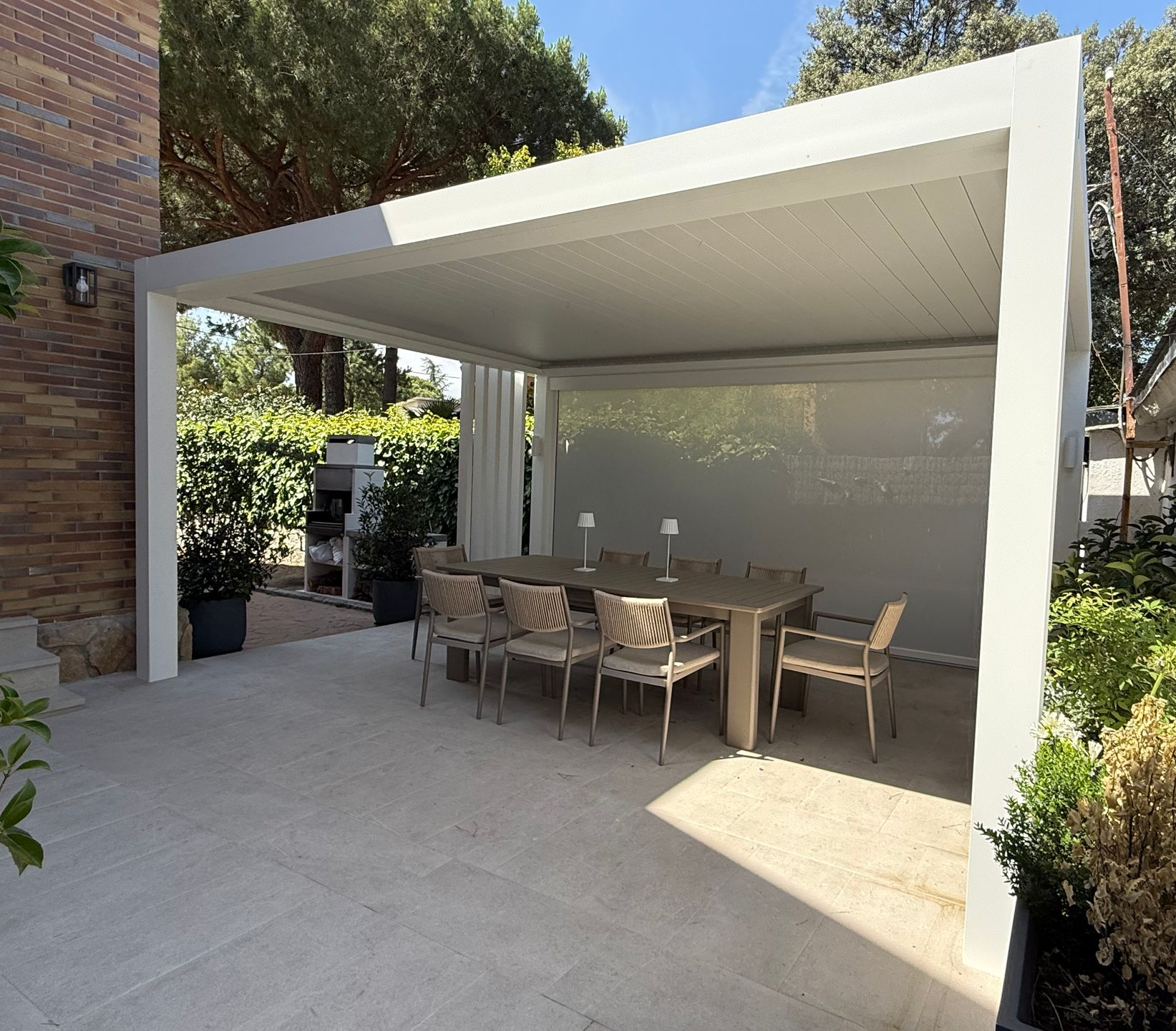 Pérgola Bioclimática en Madrid Pérgola bioclimática en Madrid, mesa, sillas y vista a una casa con piscina.