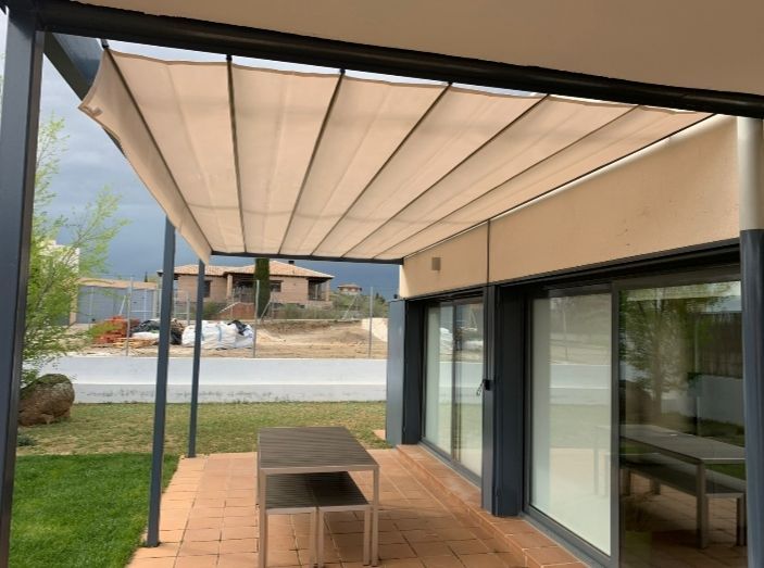 Pérgola con mesa de comedor en un patio junto a una casa, con vistas a una piscina y al jardín.