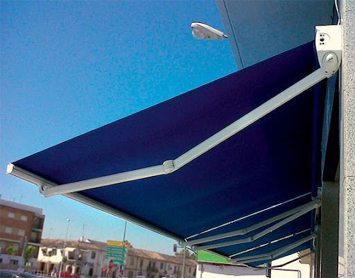 Toldo retráctil azul en el exterior de un edificio, en ángulo contra un cielo azul claro.