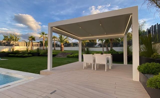 Un patio con mesa y sillas bajo una pérgola junto a una piscina.