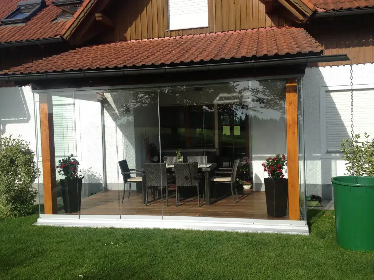 Patio exterior con paredes de vidrio, postes de madera y juego de comedor.