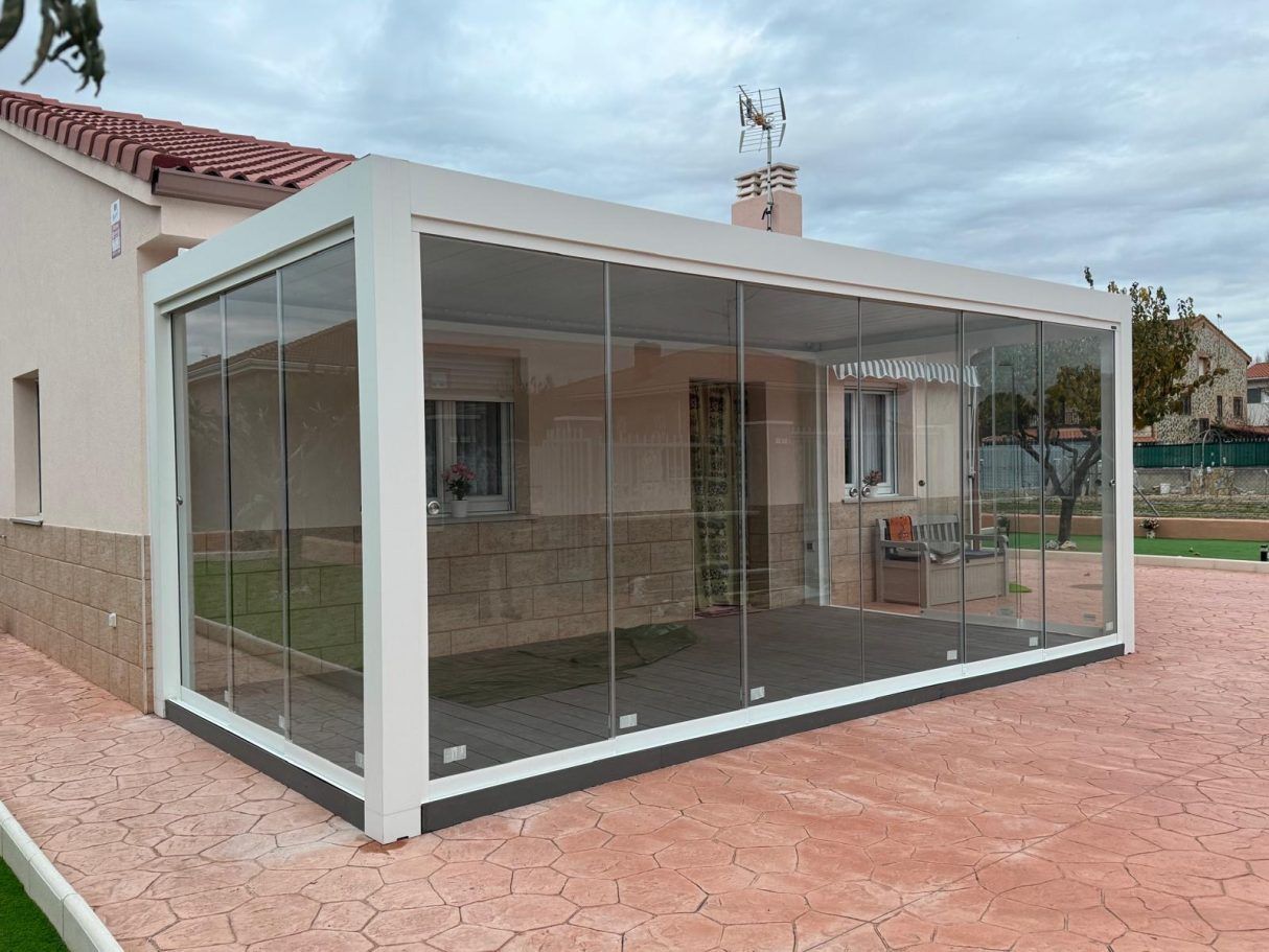 Ampliación de patio acristalado de una casa con estructura blanca y pavimento de color marrón rojizo.