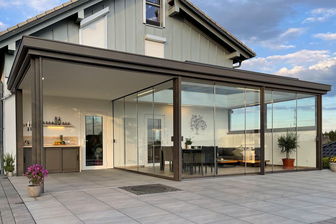 Casa con techo gris, patio con paredes de vidrio, cocina al aire libre y patio de piedra;