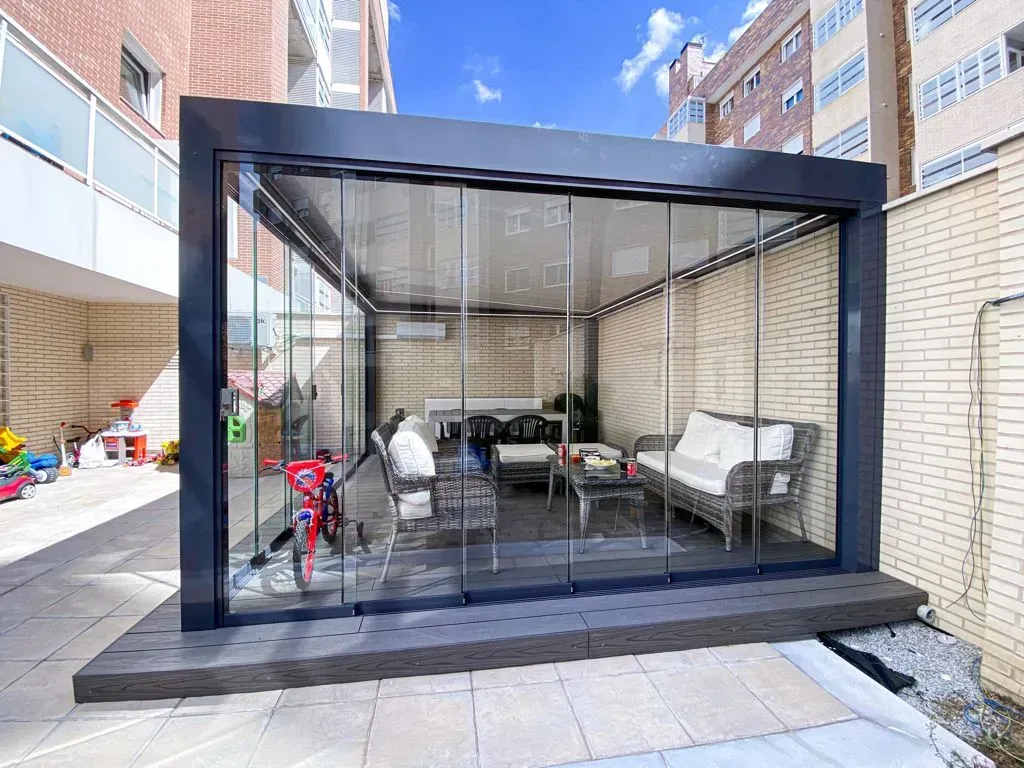 Moderna terraza acristalada con zona de estar, ubicada en una terraza elevada, al lado de un edificio de ladrillo.