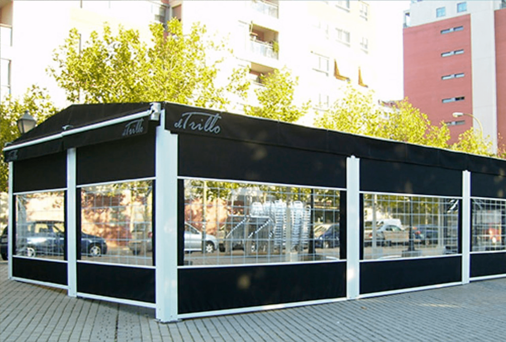 Comedor exterior en blanco y negro con ventanas transparentes. Edificio, coches y árboles visibles.