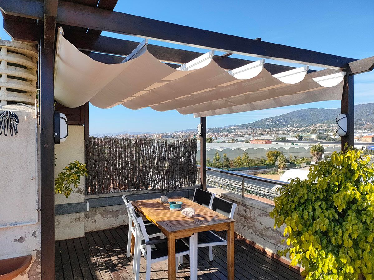 Patio en la azotea con sombrilla retráctil, mesa, sillas y vista a la ciudad.