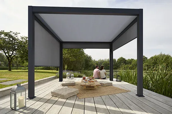 Pérgola moderna con sombra retráctil, pareja sentada en el interior, entorno al aire libre.
