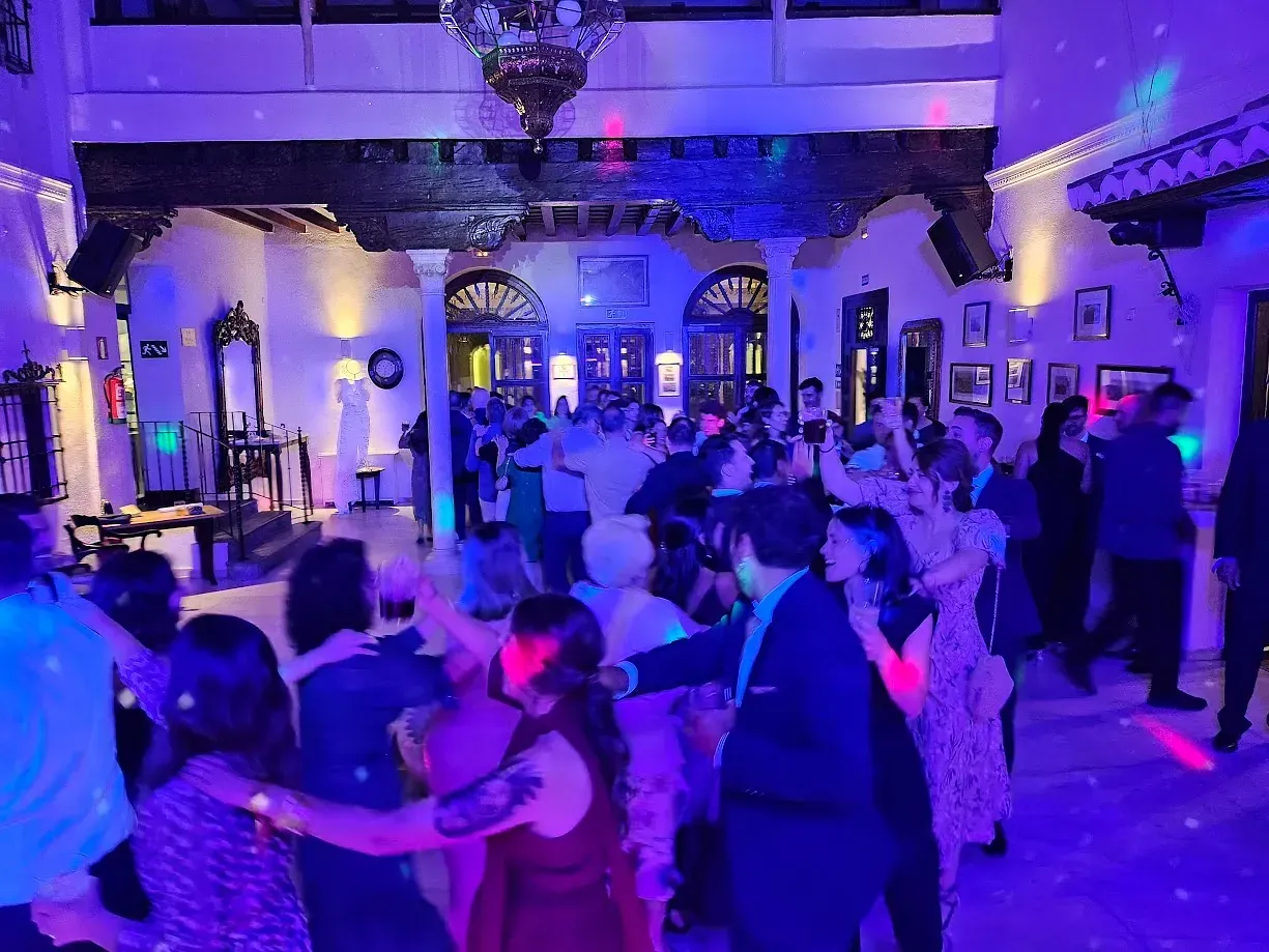 Un grupo grande de personas está bailando en una habitación con luces violetas.