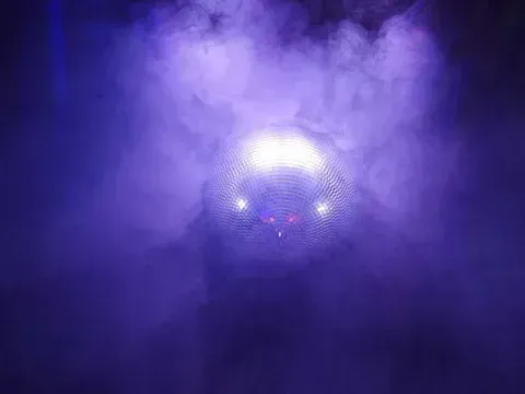 Una bola de discoteca está rodeada de humo y luces en una habitación oscura.