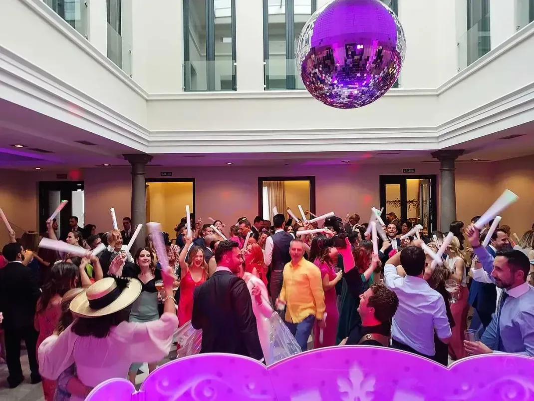 Un grupo grande de personas está bailando en una habitación con una bola de discoteca colgando del techo.