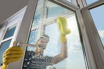 Ein Mann mit gelben Handschuhen putzt ein Fenster mit einem Schwamm.