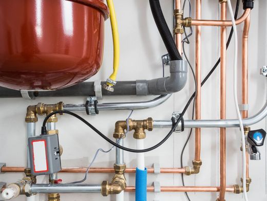 Electricista con ropa de trabajo verde que usa un destornillador para trabajar en un panel eléctrico con cables e interruptores.