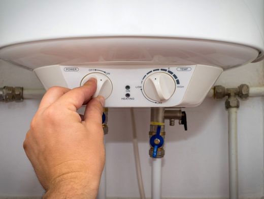 Electricista con ropa de trabajo verde que usa un destornillador para trabajar en un panel eléctrico con cables e interruptores.